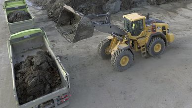 Grävmaskin lastar jordmassor på lastbilsflak, inne på anläggning