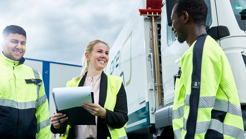 Three persons with security vest are discussing in front of a PreZero truck