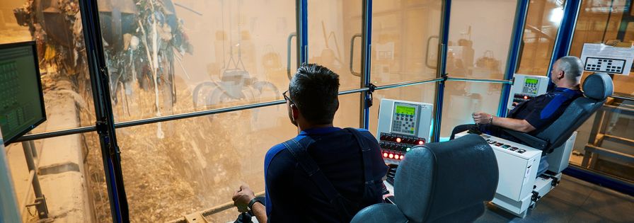 Employees control gripper arm for garbage in control room