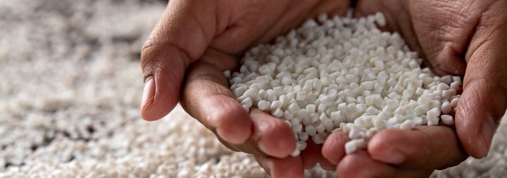 Händer som visar vita plastpellets.
