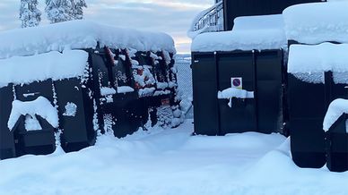 Gröna containrar med snö på och runt sig, det vill säga att snöröjning inte skötts
