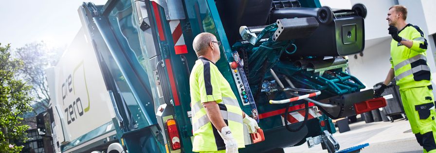 Garbage can is emptied in the garbage truck and two employee are watching the process