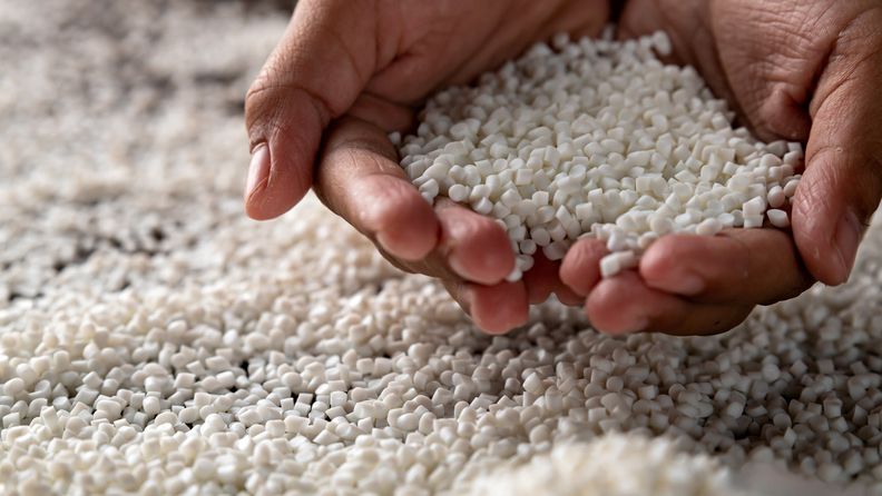Händer som visar vita plastpellets.