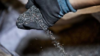 Hand im Schutzhandschuh lässt feines Metallgranulat oder Schreddergut aus dem Recycling rieseln.