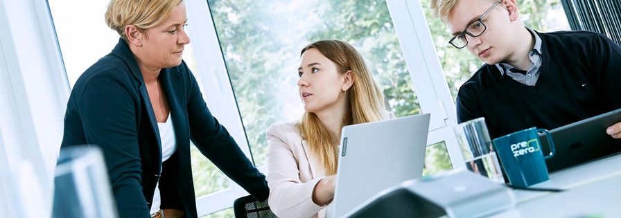 Employee shows colleagues something on laptop in the office and PreZero cup
