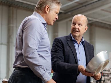 Two men in business attire inspecting a metal bowl in a large warehouse or industrial facility